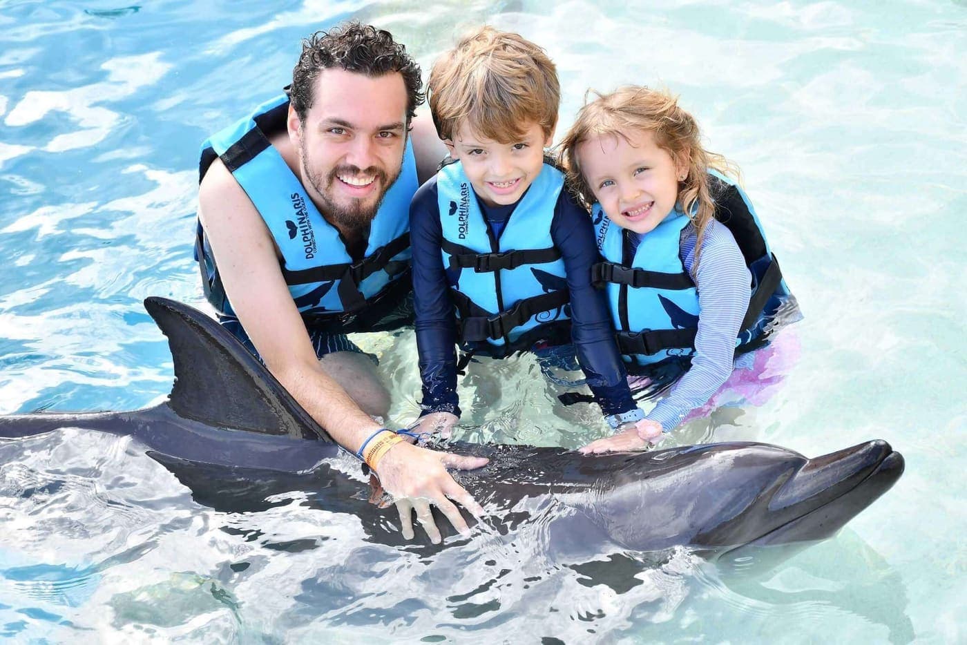 Jose and his two children in life jackets alongside two dolphins